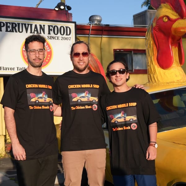 Three men in "Chicken Noodle Soup" t-shirts stand in front of The Chicken Shack restaurant.