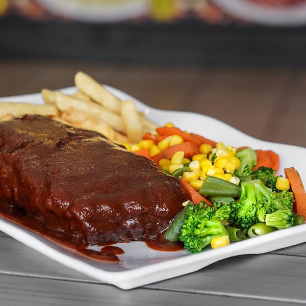 Peruvian steak with rich brown sauce, french fries, and mixed vegetables on a white plate.