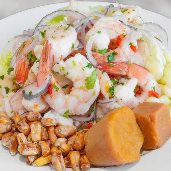 Peruvian ceviche with shrimp, white fish, red onion, cilantro, corn, and sweet potato on a white plate.