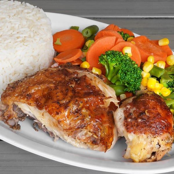 Peruvian roasted chicken with crispy skin, white rice, and mixed vegetables on a white plate.