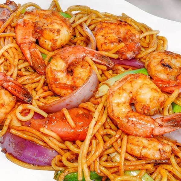 Peruvian Lomo Saltado with shrimp, noodles, red onions, and green peppers on a white plate.