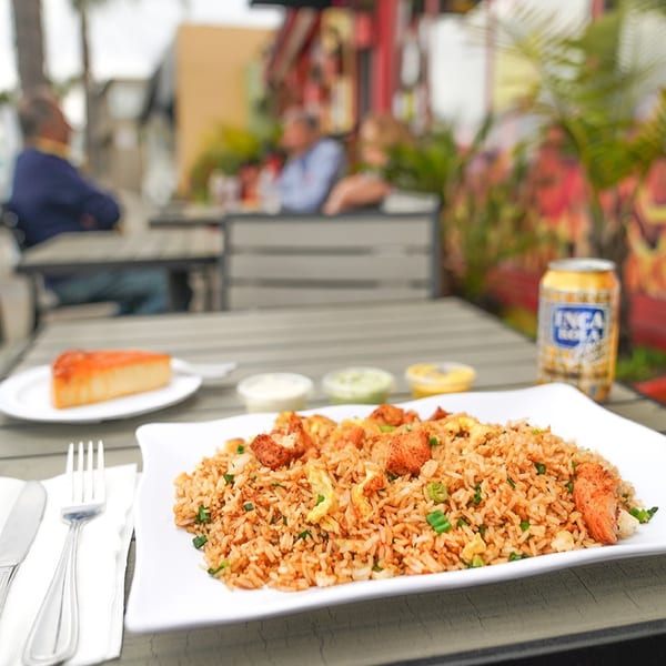 Peruvian fried rice with chicken, a slice of cake, and Inca Kola on an outdoor table.