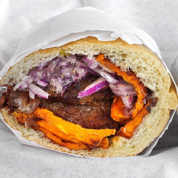 Peruvian sandwich with roasted pork, sweet potato, and red onion relish on a roll.