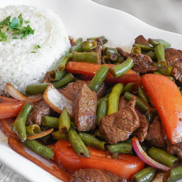 Peruvian Lomo Saltado with beef, green beans, red peppers, and onions, served with white rice.