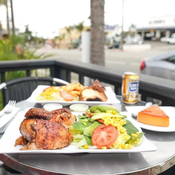 Peruvian roasted chicken with salad, fries, and flan on an outdoor patio table.