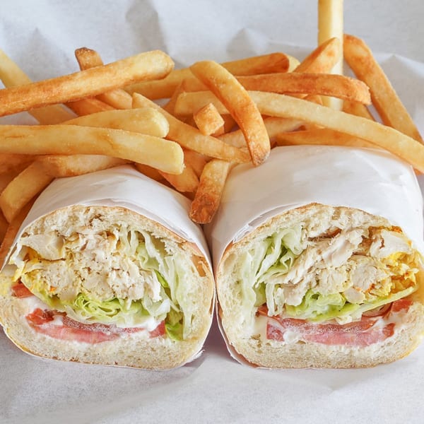 Two halves of a Peruvian chicken sandwich with lettuce, tomato, and mayo, served with fries.