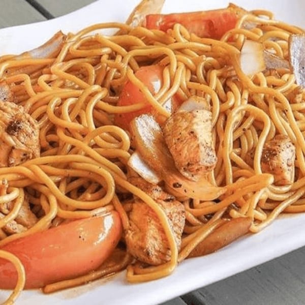 Close-up of a plate of Lomo Saltado, featuring noodles, chicken, tomatoes, and onions.
