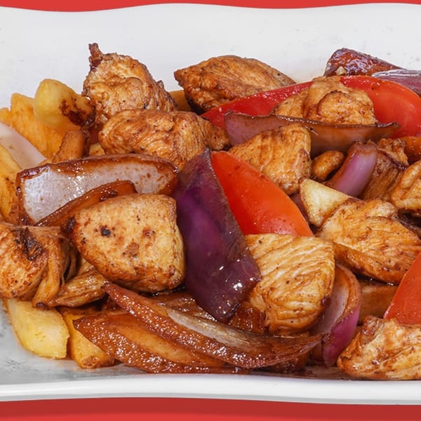 Peruvian Lomo Saltado with chicken, red onions, bell peppers, and french fries on a white plate.