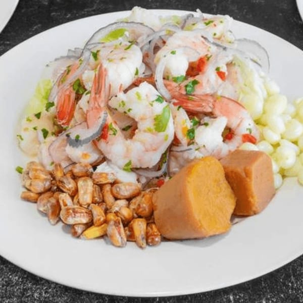 Shrimp ceviche with red onion, cilantro, sweet potato, toasted corn, and hominy on a white plate.