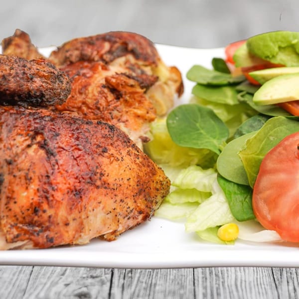 Peruvian roasted chicken with crispy skin, served with a fresh green salad, avocado, and tomato.