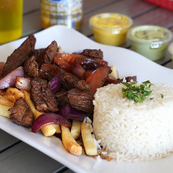 Peruvian Lomo Saltado with beef, red onions, tomatoes, fries, and white rice on a white plate.